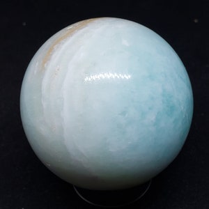 May include: A smooth, light blue and white sphere made of polished agate. The sphere has a swirling pattern of white and light blue.