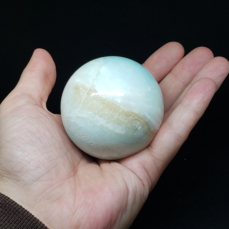 May include: A smooth, light blue and white agate sphere with brown banding. The sphere is about the size of a baseball.