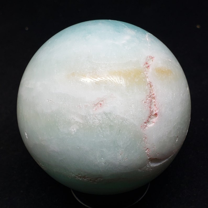 May include: A smooth, light blue sphere with white and pink veins. The sphere is made of polished stone and has a glossy finish.