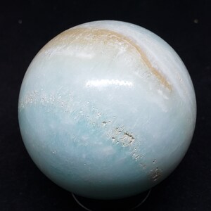 May include: A smooth, light blue sphere with a white and brown swirl pattern. The sphere is made of polished stone and has a glossy finish.