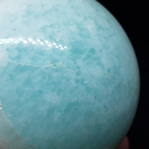 May include: A smooth, light blue sphere with a mottled, cloudy pattern. The sphere is made of polished stone.