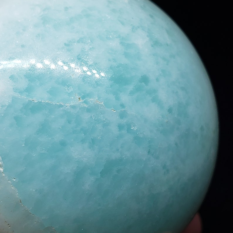May include: A smooth, light blue sphere with a mottled, cloudy pattern. The sphere is made of polished stone.