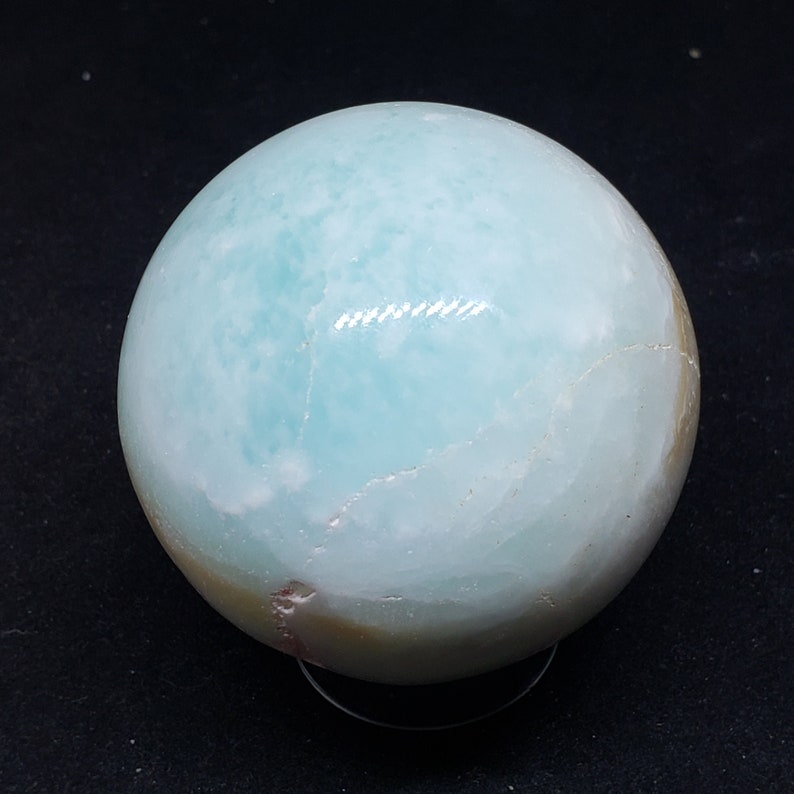 May include: A light blue and white agate sphere with a smooth, polished surface. The sphere is sitting on a clear stand.