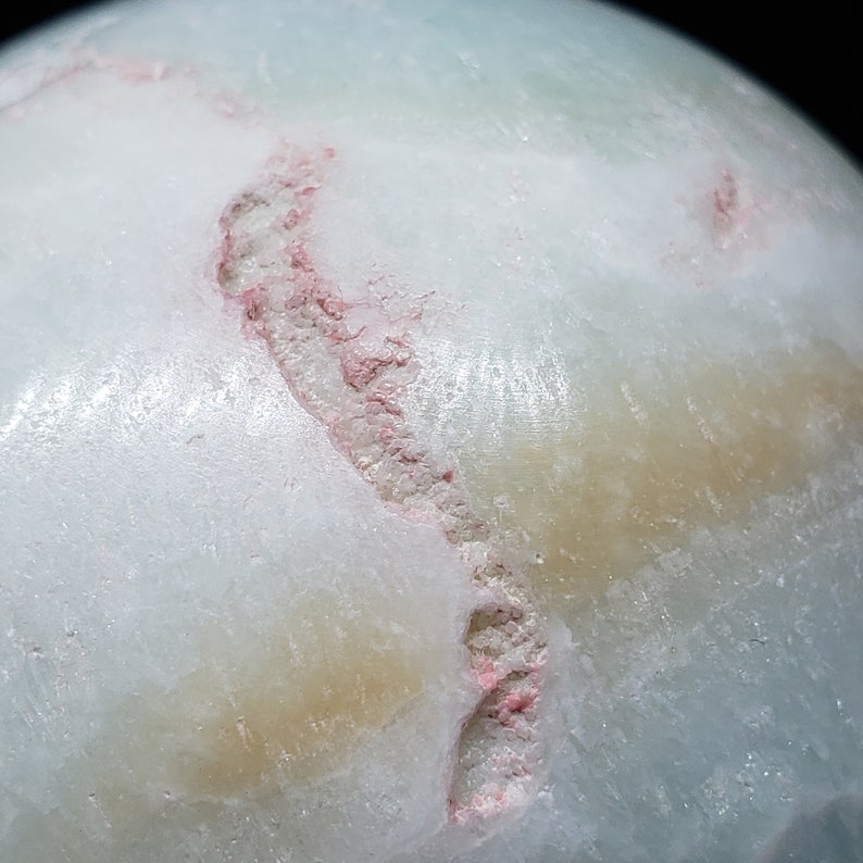 May include: Close-up of a white, green, and pink sphere with a crack running through it. The sphere has a smooth, polished surface.