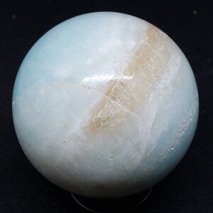 May include: A smooth, light blue and white sphere with brown veins. The sphere is made of polished stone and has a glossy finish.