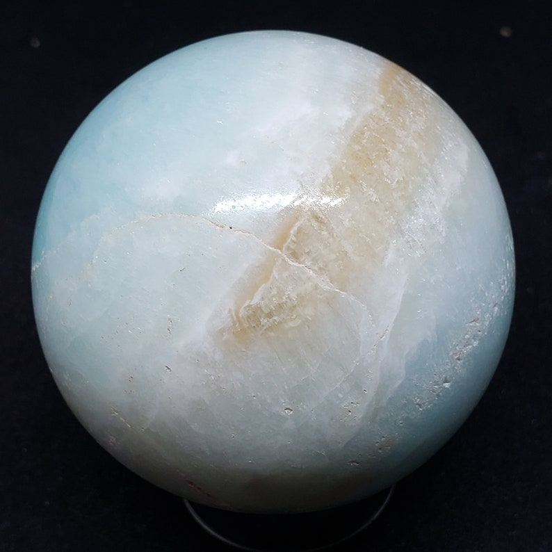 May include: A smooth, light blue and white sphere with brown veins. The sphere is made of polished stone and has a glossy finish.