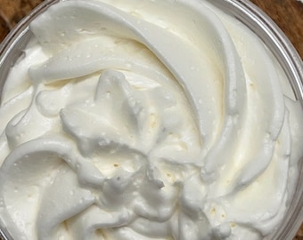 Peut inclure: Gros plan sur un beurre corporel fouetté blanc dans un récipient en plastique transparent. Le beurre est lisse et crémeux, avec un motif en spirale sur le dessus.