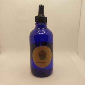 Op de afbeelding: Een blauwe glazen fles met een druppelaar en een bruin etiket met de tekst "OzonedOrganics.com". Het etiket heeft een afbeelding van een bloem met een wereldbol erin.