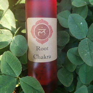 以下が含まれることがあります： 赤いガラス製のローラーボトル。茶色のラベルには「Root Chakra」と赤いシンボルが書かれています。ボトルは緑色のクローバーの葉で囲まれています。