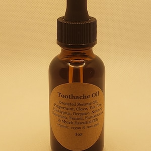 May include: A brown glass bottle with a dropper top and a label that reads "Toothache Oil". The label lists the ingredients: Ozonated Sesame Oil, Peppermint, Clove, Tea Tree, Eucalyptus, Oregano, Nutmeg, Cinnamon, Fennel, Frankincense & Myrrh Essential Oils. The label also states that the oil is organic, vegan, and non-GMO. The bottle contains 30 ml of oil.