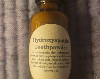 May include: A small amber glass bottle with a black lid containing Hydroxyapatite Toothpowder. The label lists the ingredients: calcium bentonite clay, hydroxyapaptite powder, di-calcium phosphate, diatomaceous earth, baking soda, calcium carbonate, sage leaf, Himalayan salt, maca, lucuma, activated charcoal, turmeric powder. The bottle is labeled with a net weight of 1 oz.