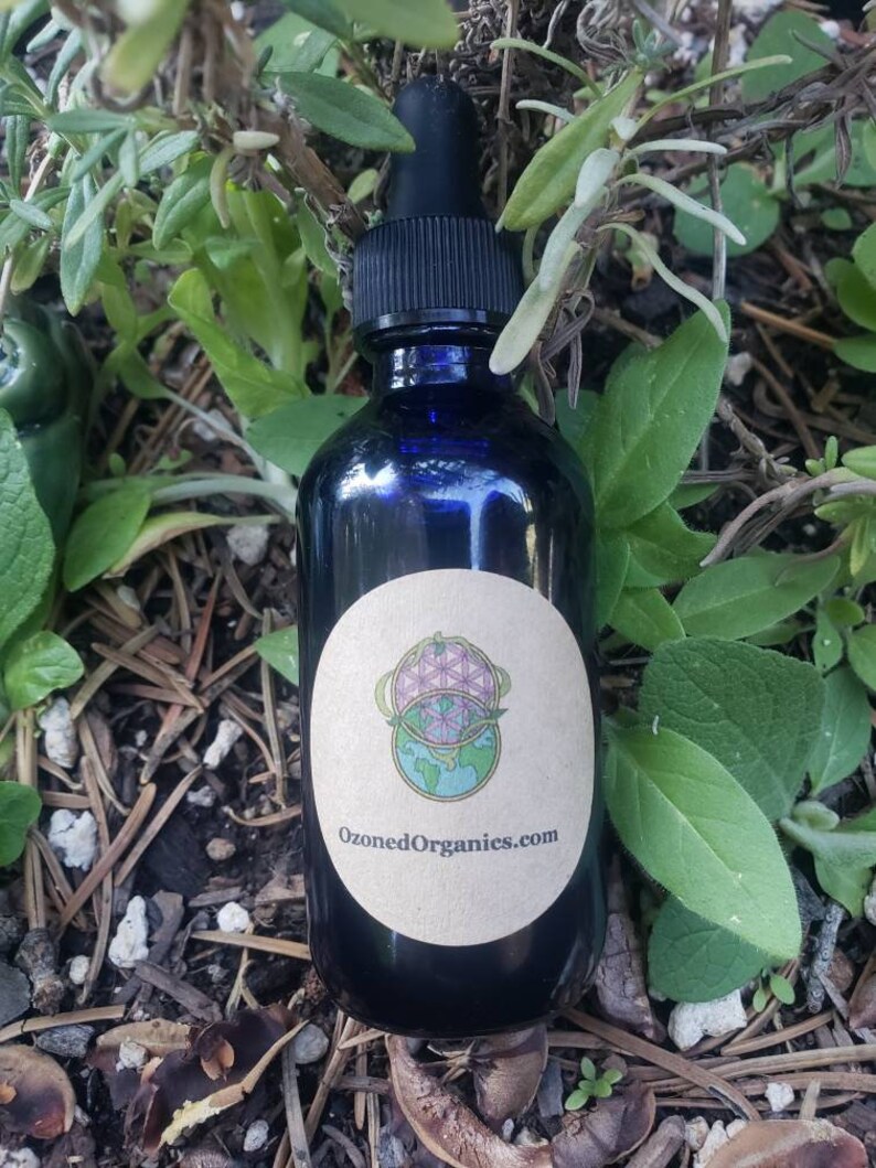 May include: A blue glass bottle with a dropper top and a brown label. The label has a graphic of a globe with a flower of life design and the text "OzonedOrganics.com".