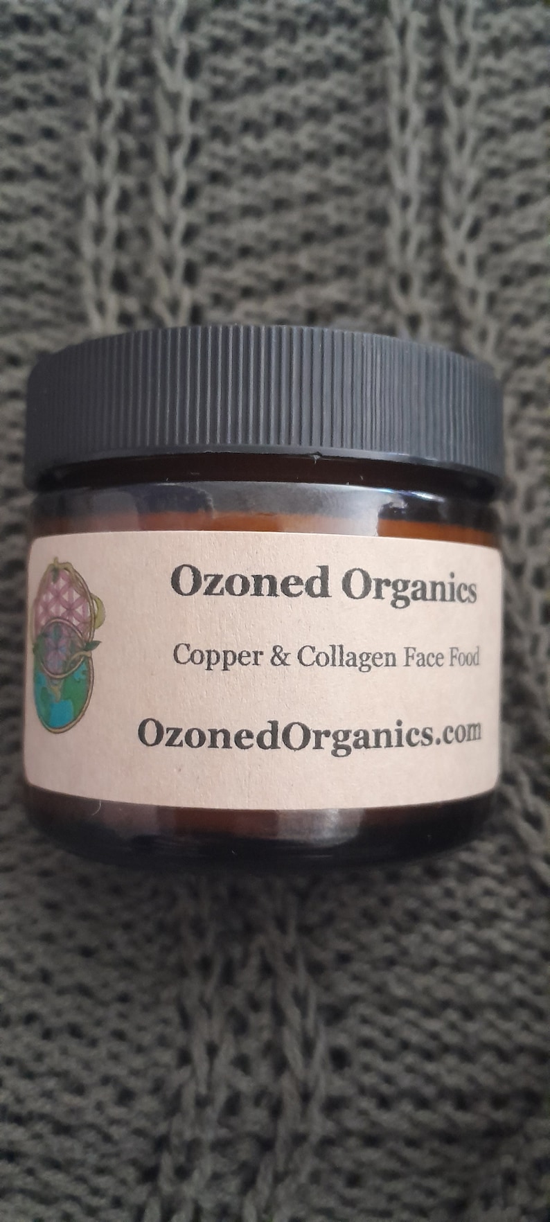 Op de afbeelding: Een bruine glazen pot met een zwarte deksel en een wit etiket. Het etiket luidt "Ozoned Organics Copper & Collagen Face Food OzonedOrganics.com".