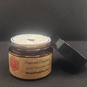 Könnte beinhalten: Ein kleines Glasgefäß mit einem braunen Etikett, auf dem "Ozoned Organics Sacral Chakra Skin Food ozonedorganics.com" steht. Das Gefäß enthält eine weiße Creme und hat einen schwarzen Deckel.