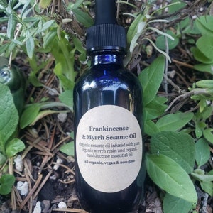May include: A dark blue glass bottle with a dropper top and a white label that reads "Frankincense & Myrrh Sesame Oil". The label also includes the text "Organic sesame oil infused with pure organic myrrh resin and organic frankincense essential oil. All organic, vegan & non-gmo."