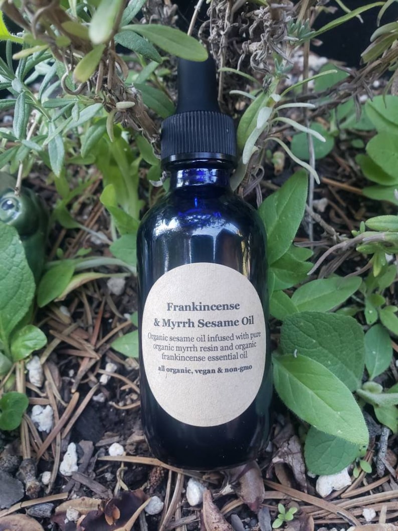 May include: A dark blue glass bottle with a dropper top and a white label that reads "Frankincense & Myrrh Sesame Oil". The label also includes the text "Organic sesame oil infused with pure organic myrrh resin and organic frankincense essential oil. All organic, vegan & non-gmo."
