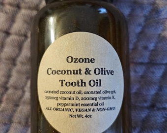 May include: A brown glass bottle with a white label that reads "Ozone Coconut & Olive Tooth Oil" and lists the ingredients: ozonated coconut oil, ozonated olive gel, 250mcg vitamin D, 200mcg vitamin K, peppermint essential oil. The label also states "All Organic, Vegan & Non-GMO" and "Net Wt. 4oz".