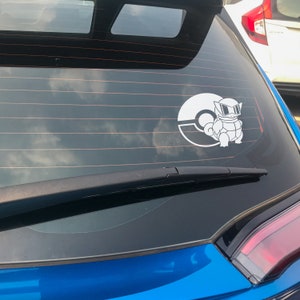 May include: A blue car with a white Pokemon sticker on the back window. The sticker features a Pokemon character with sunglasses and a Pokeball.