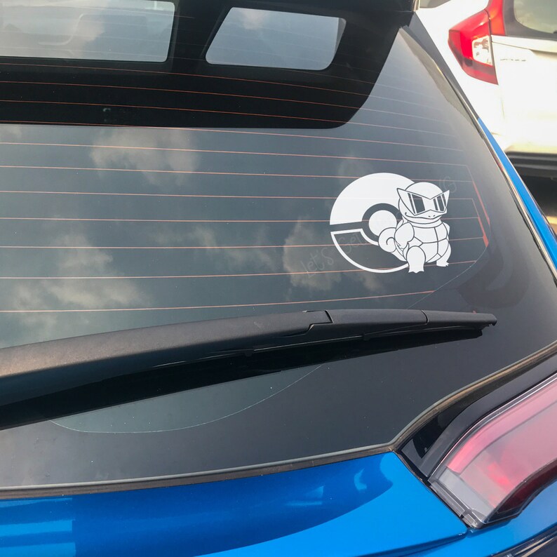 May include: A blue car with a white Pokemon sticker on the back window. The sticker features a Pokemon character with sunglasses and a Pokeball.