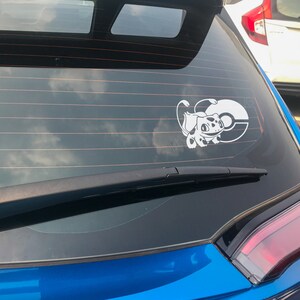 May include: A blue car with a white vinyl sticker of a Pokemon character on the back window. The sticker shows a white Pokemon character with a red spot on its back, holding a Pokeball.