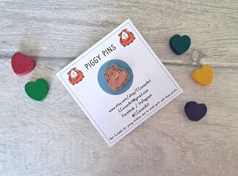May include: A brown guinea pig pin on a blue background. The pin is part of a set of piggy pins. The card reads "Piggy Pins" and includes contact information for the shop.