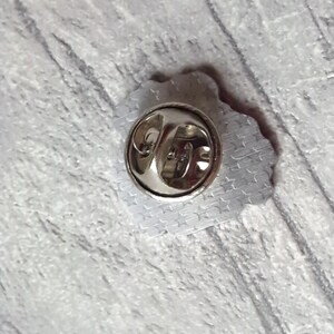 May include: The back of a silver pin with a star pattern. The pin has a metal clasp.