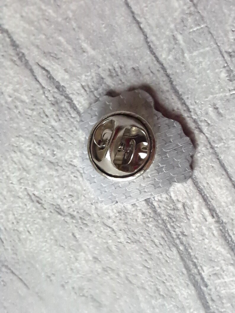 May include: The back of a silver pin with a star pattern. The pin has a metal clasp.