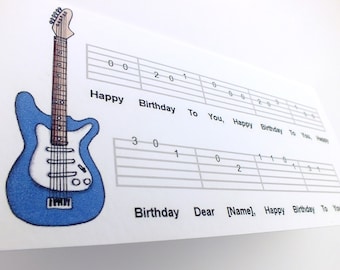Könnte beinhalten: Eine blaue E-Gitarre mit weißem Schlagbrett und einem Gitarrentab für "Happy Birthday" auf weißem Hintergrund.