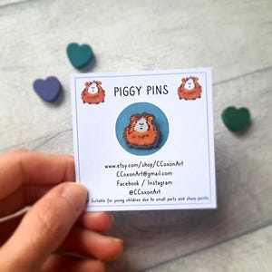 May include: A white card with the text "PIGGY PINS" and a cartoon image of a guinea pig. The card also includes contact information for the seller, including their Etsy shop, email address, and social media handles.