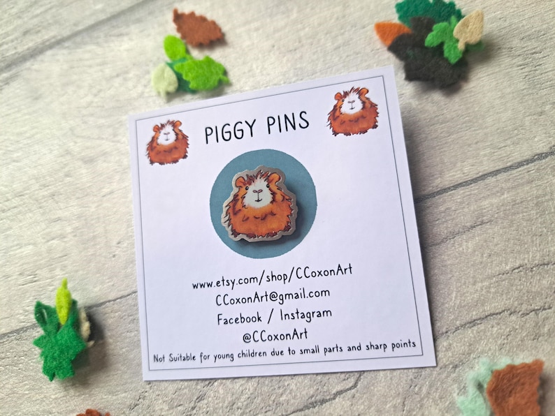 May include: A card with the text "PIGGY PINS" and contact information for the shop CCoxonArt. The card features a cartoon image of a brown and white guinea pig.