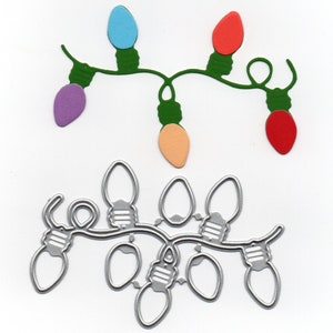 May include: A festive Christmas light strand with colorful bulbs in blue, red, purple, and peach, connected by a green wire. Below, a silver metal die-cut of a similar light strand is displayed, perfect for crafting holiday decorations.