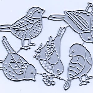 May include: A collection of five die-cut metal bird shapes in various poses. The birds have detailed etched designs, including feathers and patterns. The die cuts are silver-colored and suitable for crafting projects.