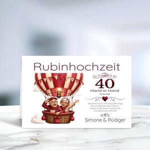 Könnte beinhalten: Eine weiße Grußkarte zur Rubinhochzeit mit einem rot-weißen Heißluftballon und einem älteren Paar darin. Der Text lautet Rubinhochzeit, 40, Hand in Hand, 25.08.2026, Simone & Rüdiger, ergänzt durch ein deutsches Gedicht über kleine Momente.