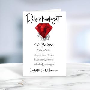 Könnte beinhalten: Eine weiße Grußkarte mit einer roten Diamant-Illustration, schwarzen floralen Akzenten und dem schwarzen Text "Rubinhochzeit 40 Jahre Seite an Seite, mit gemeinsamen Wegen, besonderen Momenten und vielen Erinnerungen. Lisbeth & Werner" auf der Vorderseite.