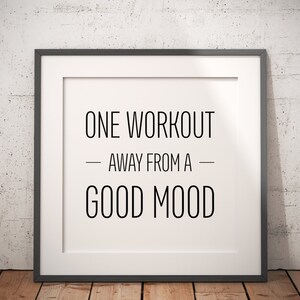 May include: A framed motivational quote that reads "One workout away from a good mood". The frame is black and the background is a white brick wall.