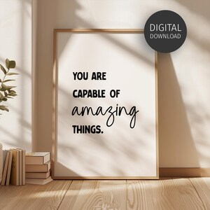 May include: A vertical rectangular framed wall art piece featuring the black text YOU ARE CAPABLE OF amazing THINGS. A circular black badge in the upper right corner contains the white text DIGITAL DOWNLOAD. The frame is light wood.