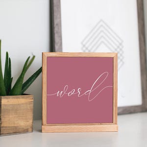 May include: A wooden framed sign with a pink background and the word "word" written in white cursive script.