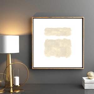May include: A framed abstract painting with two beige brushstrokes on a white background. The frame is gold and the painting is hanging on a gray wall.