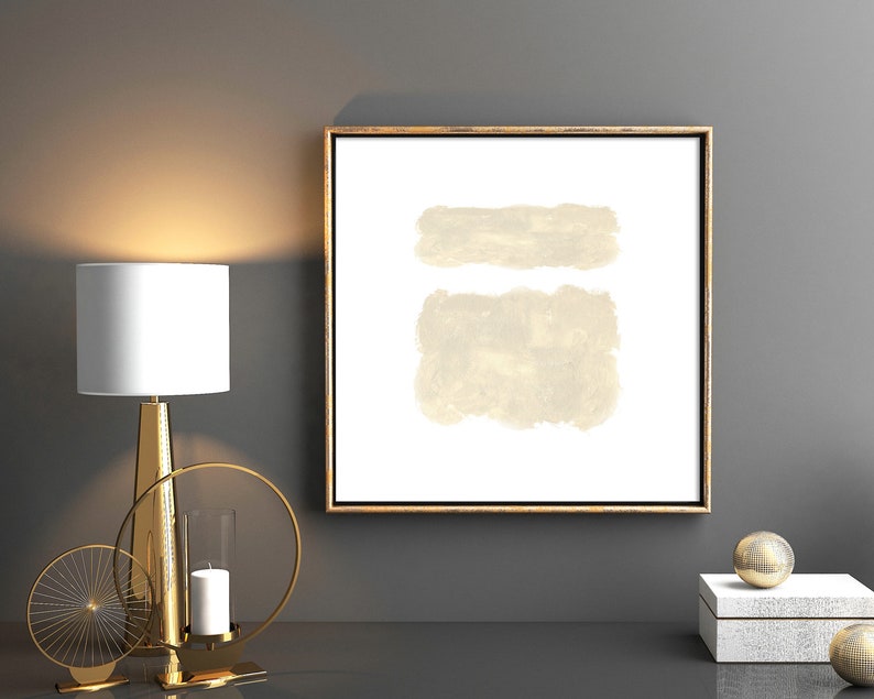 May include: A framed abstract painting with two beige brushstrokes on a white background. The frame is gold and the painting is hanging on a gray wall.
