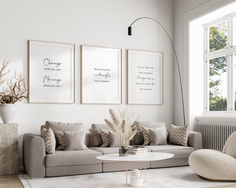 K&ouml;nnte beinhalten: Drei gerahmte inspirierende Zitate an einer wei&szlig;en Wand in einem Wohnzimmer. Die Zitate lauten: "Ver&auml;ndere, was du kannst, manage, was du nicht kannst", "Verletzlich zu sein ist eine St&auml;rke, keine Schw&auml;che", und "Du bist mutiger, als du glaubst, st&auml;rker, als du scheinst, und kl&uuml;ger, als du denkst."