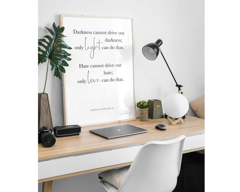 Pode incluir: Uma impress&atilde;o emoldurada com fundo branco e texto preto. O texto diz "Darkness cannot drive out darkness; only light can do that. Hate cannot drive out hate; only love can do that." A cita&ccedil;&atilde;o &eacute; atribu&iacute;da a Martin Luther King Jr. A impress&atilde;o est&aacute; em uma mesa com um laptop, uma l&acirc;mpada e uma planta.