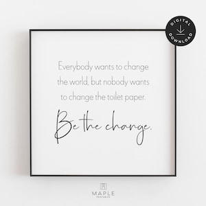 This image shows a framed square print featuring the quote: "Everybody wants to change the world, but nobody wants to change the toilet paper. Be the change." The bathroom print features black text on a clean white background and is displayed in a black frame. A small circle in the corner says “Digital Download.”