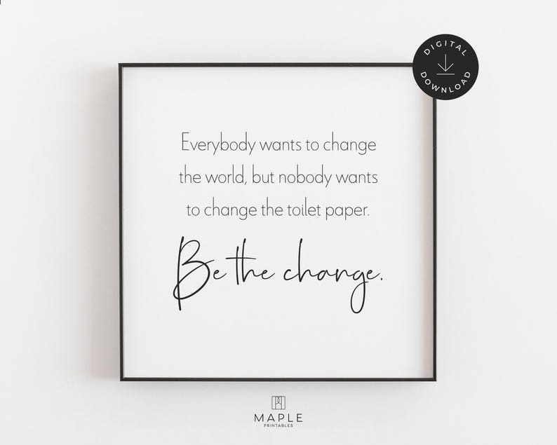 This image shows a framed square print featuring the quote: "Everybody wants to change the world, but nobody wants to change the toilet paper. Be the change." The bathroom print features black text on a clean white background and is displayed in a black frame. A small circle in the corner says “Digital Download.”