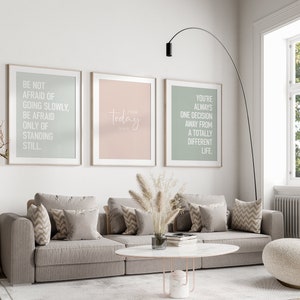 May include: Three framed motivational posters with white text on a light background. The posters are hanging on a white wall above a gray couch with pillows. The text on the posters reads: "Be not afraid of going slowly, be afraid only of standing still."  "Today is the day."  "You're always one decision away from a totally different life."