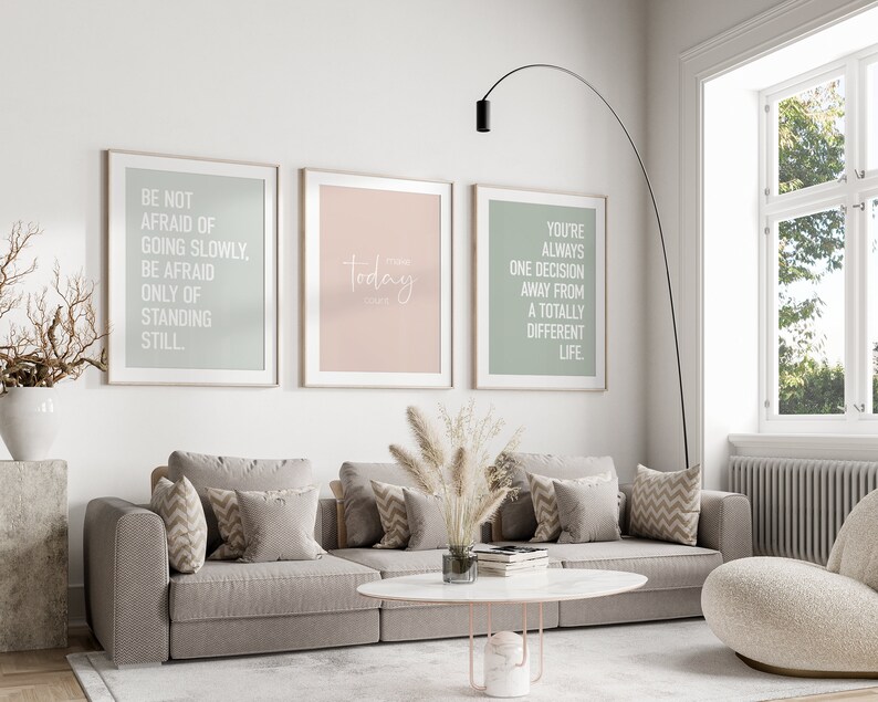May include: Three framed motivational posters with white text on a light background. The posters are hanging on a white wall above a gray couch with pillows. The text on the posters reads: "Be not afraid of going slowly, be afraid only of standing still."  "Today is the day."  "You're always one decision away from a totally different life."