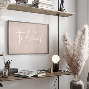Może przedstawiać: Wydruk w ramie z r&oacute;żowym tłem i białym tekstem, kt&oacute;ry brzmi "make today count", wiszący na ścianie nad drewnianym biurkiem z lampą, wazą z suszoną trawą pampasową i książką.