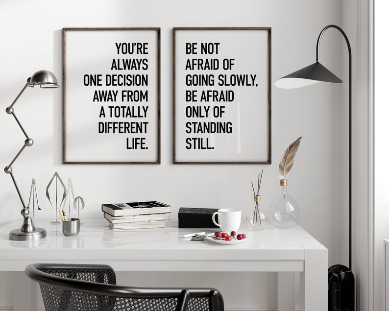 May include: Two black framed motivational posters with white text. The left poster says "You're always one decision away from a totally different life." The right poster says "Be not afraid of going slowly, be afraid only of standing still."