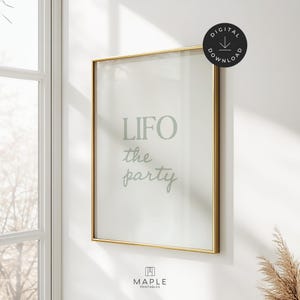 以下が含まれることがあります： 「LIFO the party」というテキストが薄緑色の筆記体で書かれたフレームプリント。 金色のフレームが白い背景を囲んでいます。 プリントは窓の近くの白い壁に掛けられています。