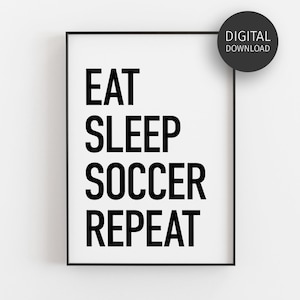 May include: A rectangular wall art print in a thin black frame featuring the black text EAT SLEEP SOCCER REPEAT on a white background. A circular black badge in the upper right corner contains the white text DIGITAL DOWNLOAD.