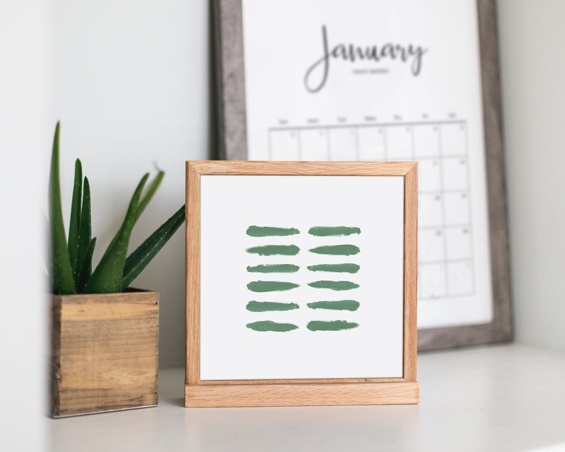 May include: A framed print with a minimalist design featuring a series of green brushstrokes on a white background. The print is displayed on a wooden easel.